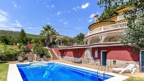 A swimming pool with a stone wall and a red building with a balcony. - Spacious, Sublime Villa just 15km to Barcelona! (Torrelles de Llobregat)