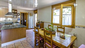 A kitchen with a wooden island, a dining table with chairs, a window with curtains, and a built-in oven. - Spacious, Sublime Villa just 15km to Barcelona! (Torrelles de Llobregat)