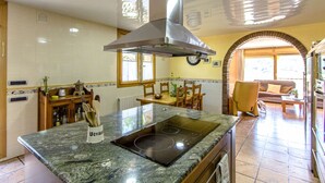 A kitchen with a central island, a stove, and a ventilation hood. There is a dining area with a table and chairs, and a living room with a sofa and a coffee table. - Spacious, Sublime Villa just 15km to Barcelona! (Torrelles de Llobregat)