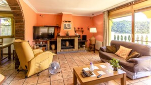 A living room with a fireplace, sofa, armchair, and a television. - Spacious, Sublime Villa just 15km to Barcelona! (Torrelles de Llobregat)
