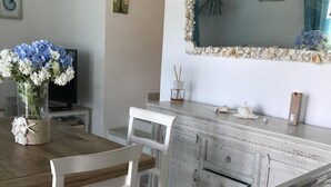 Ein Essbereich mit einem Holztisch, weißen Stühlen, einer weißen Kommode mit Schubladen und einem Spiegel mit Muschelbildung.