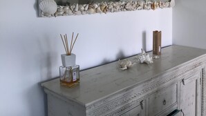 Ein Spiegel mit Muschelrahmen, ein weißes Schränkchen mit Schubladen und eine kleine Vase mit Schilf.