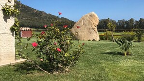 Ein gepflegter Rasen mit einem großen Felsen, einem blühenden Strauch und einem Gebäude mit Steinverkleidung.