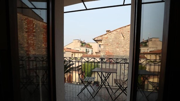 A balcony with a view of old buildings, a metal railing, and a table with chairs.