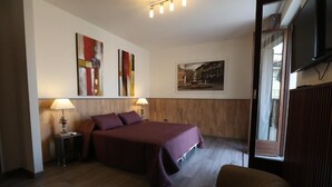A hotel room with a bed, two bedside tables with lamps, a TV, and artwork on the walls.