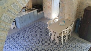 Cozinha compacta com parede de pedra, pia, armários e área de jantar com piso estampado.