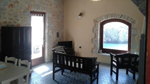 Quarto com parede de pedra, um banco de madeira, uma mesa e vista pela janela arqueada.