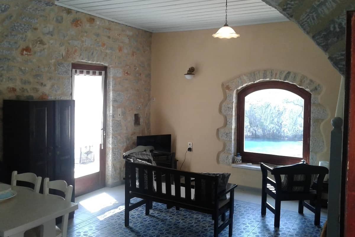 A room with a stone wall, a wooden bench, a table, and a view through an arched window.