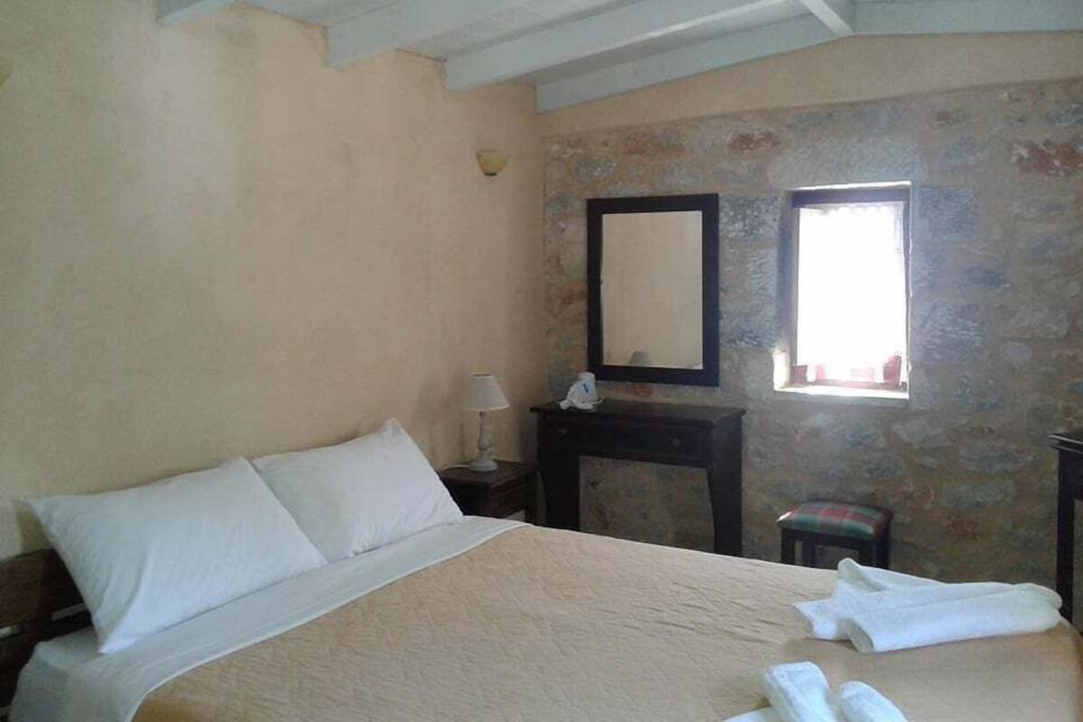 A bedroom with a bed, a nightstand, a lamp, a mirror, and a window.