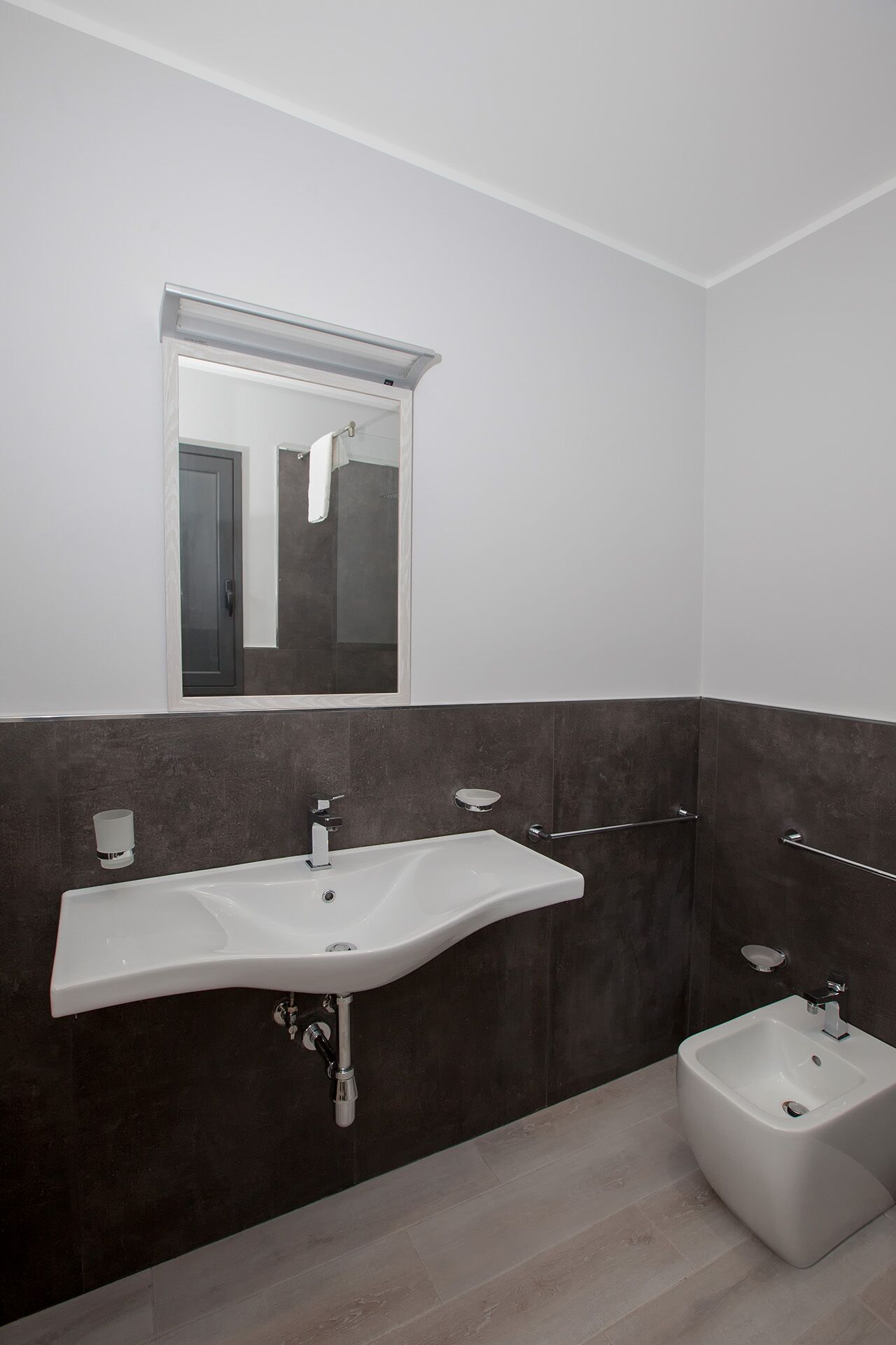 Une salle de bain moderne avec un grand lavabo blanc, un petit bidet et un miroir au-dessus du lavabo.