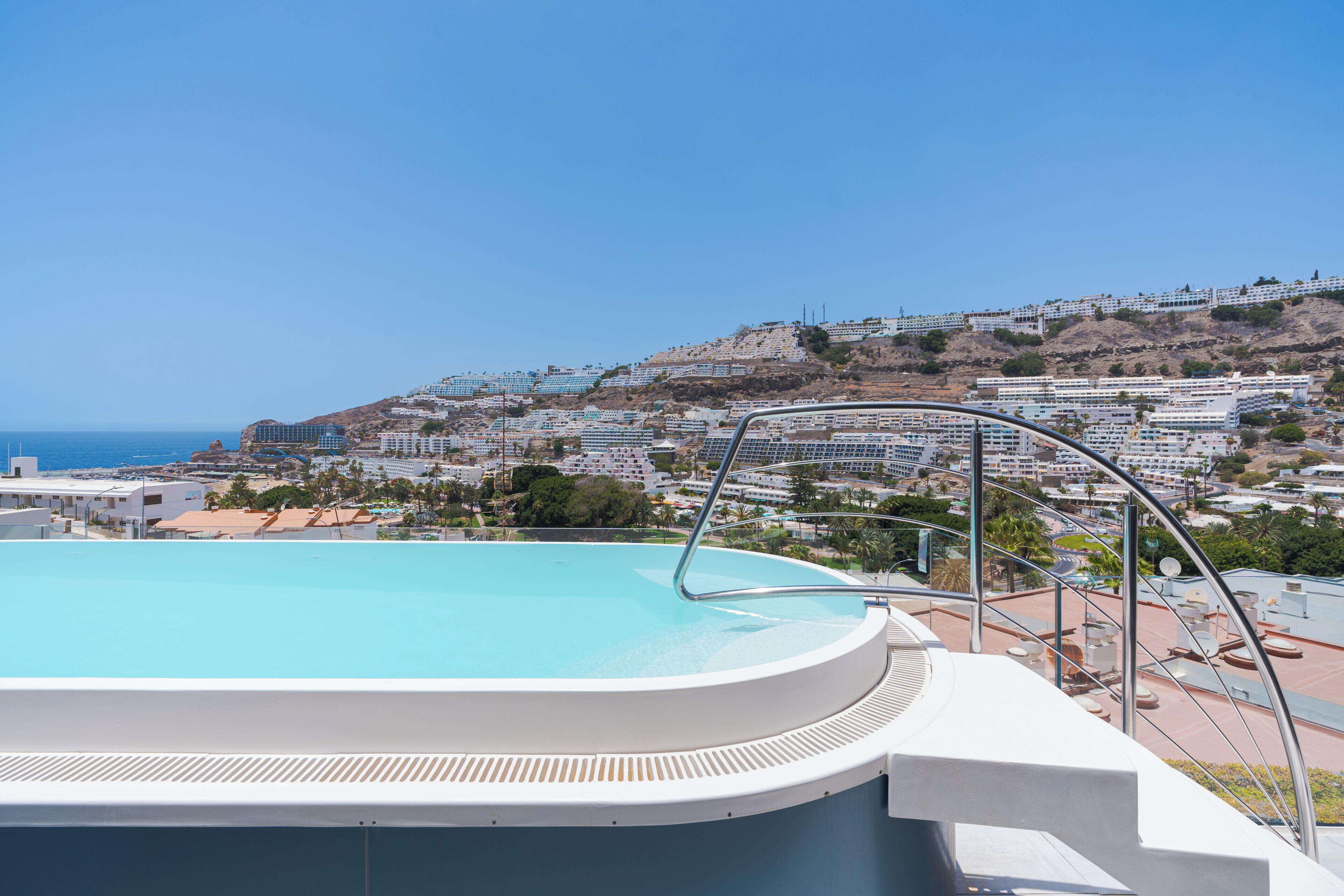 A swimming pool with a view of a coastal town and hills.