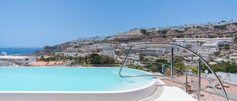 A swimming pool with a view of a coastal town and hills.
