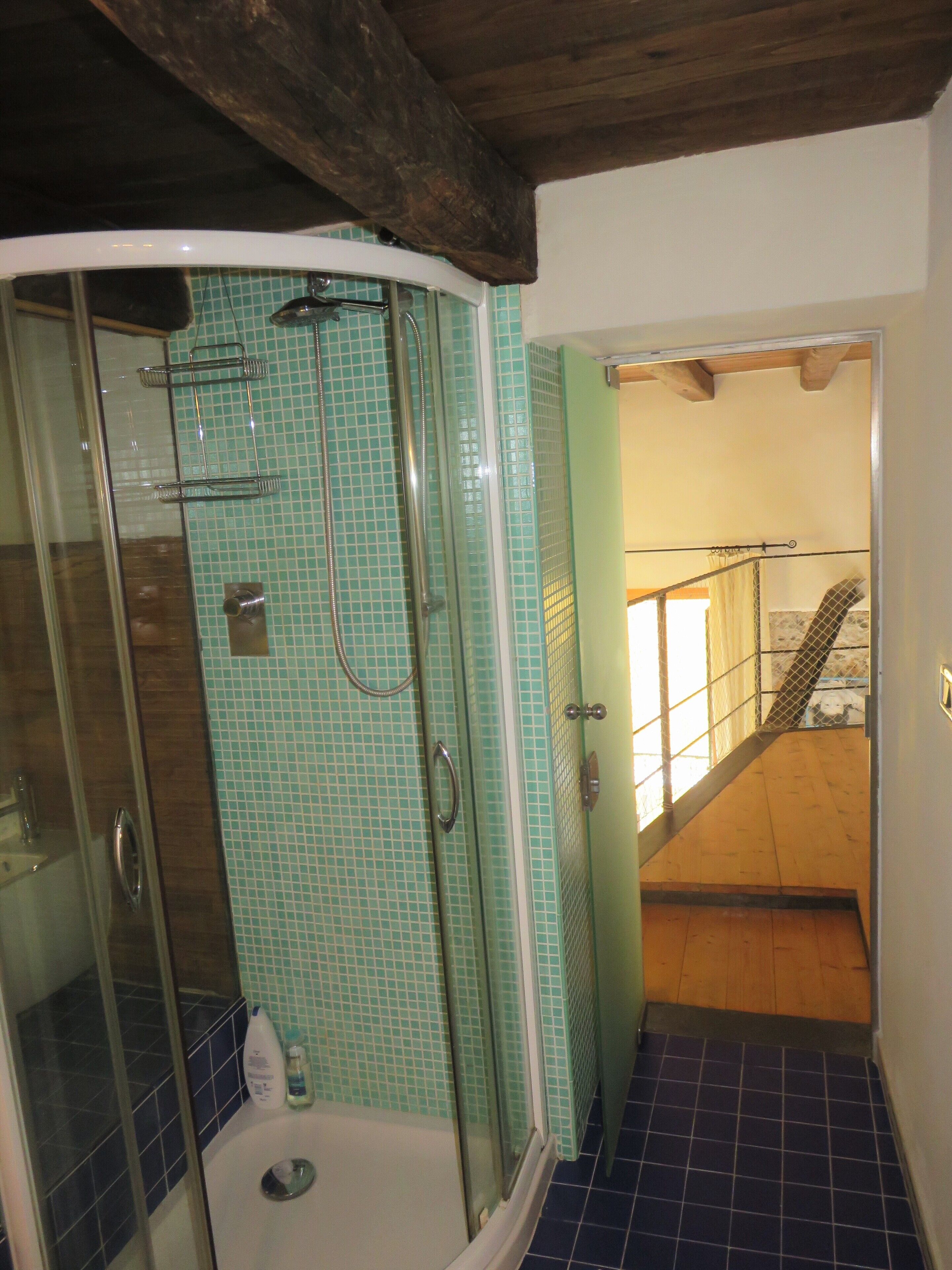 A bathroom with a glass-enclosed shower, tiled walls, and a wooden staircase leading to an upper level.