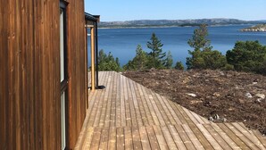 A wooden deck leading to a building with a view of a lake and mountains. - New holiday home, idyllically located by the sea (Kolvereid)