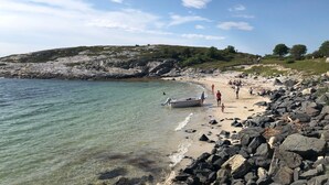 A rocky beach with clear water, a boat on the shore, and people walking. - New holiday home, idyllically located by the sea (Kolvereid)