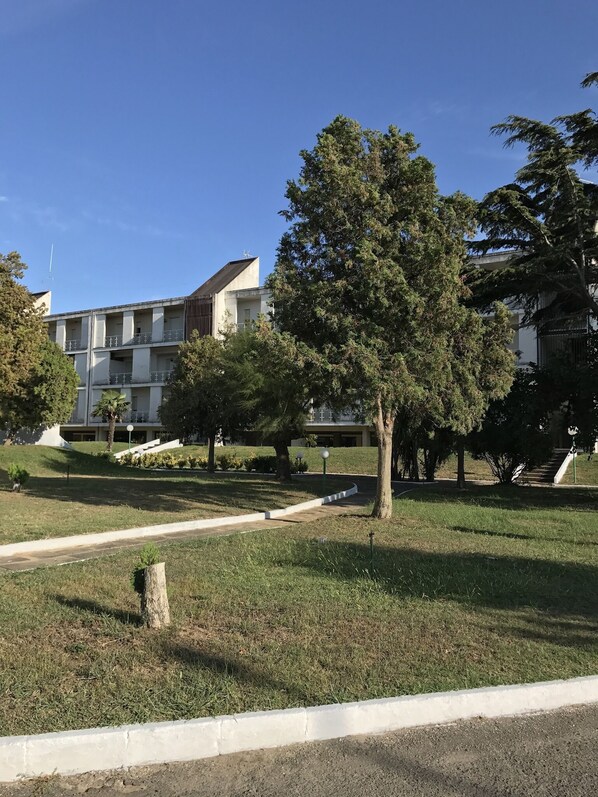 A residential building with a flat roof, multiple balconies, and a well-maintained lawn with trees.