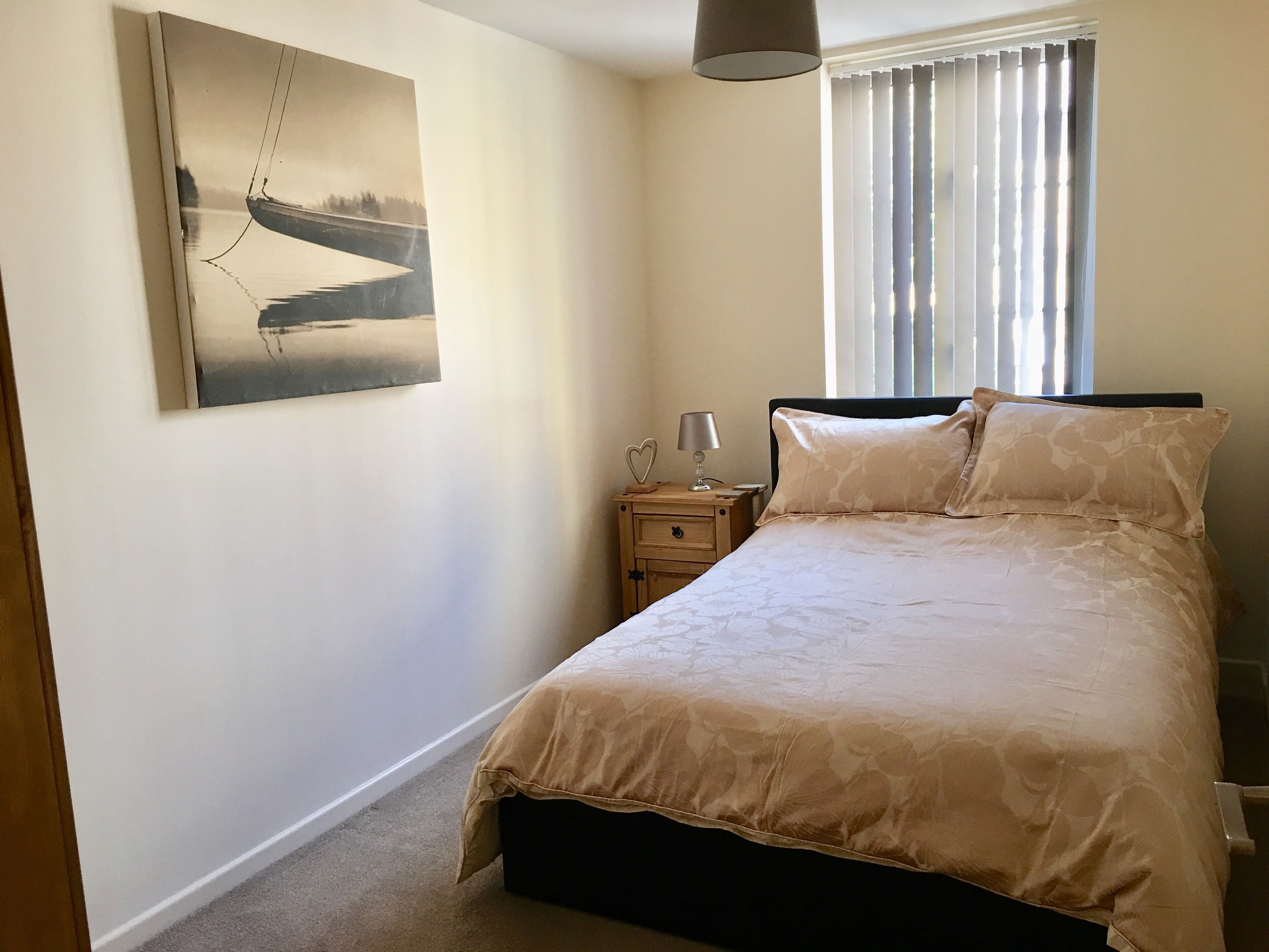 Une chambre à coucher avec un lit, une table de chevet, une lampe, un tableau et une fenêtre avec des stores.