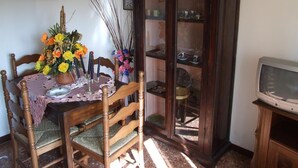Un comedor con una mesa de madera, sillas, un armario con puertas de cristal y un televisor sobre un mueble bajo.