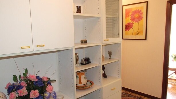 Un pasillo con estanterías blancas, un jarrón de flores y un cuadro en la pared.