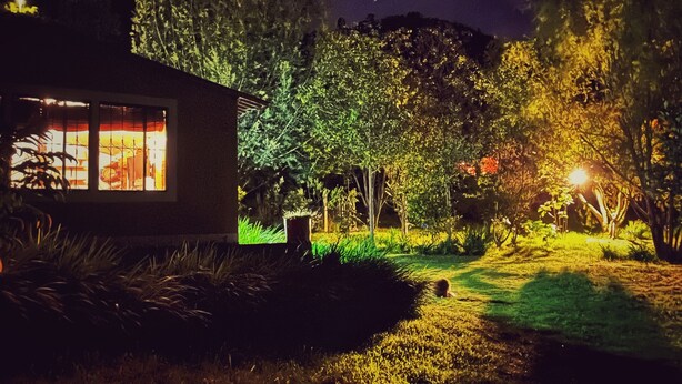 Une maison dont l’intérieur est éclairé, entourée d’un jardin la nuit.