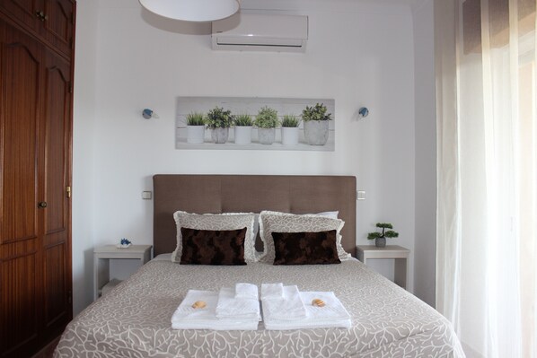Een netjes ingerichte slaapkamer met een bed, twee nachtkastjes, een wandplank met planten en een houten garderobe.