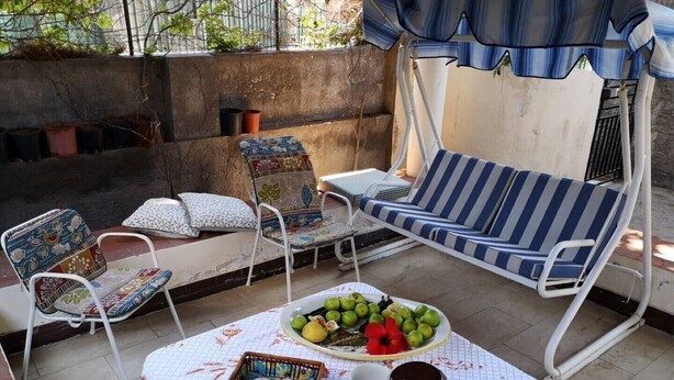 Un patio con una mesa dispuesta para comer, que incluye pan, frutas y una jarra de bebida.