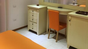 Una habitación con cama, escritorio, silla, espejo y unidad de aire acondicionado.