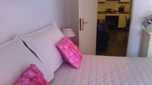 A bedroom with a bed, pillows, a lamp, and a view into the kitchen. - Freedom apartment (Portovenere)