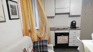 A modern kitchen with white cabinets, a coffee machine, and a dining area with a table and chairs. - Freedom apartment (Portovenere)