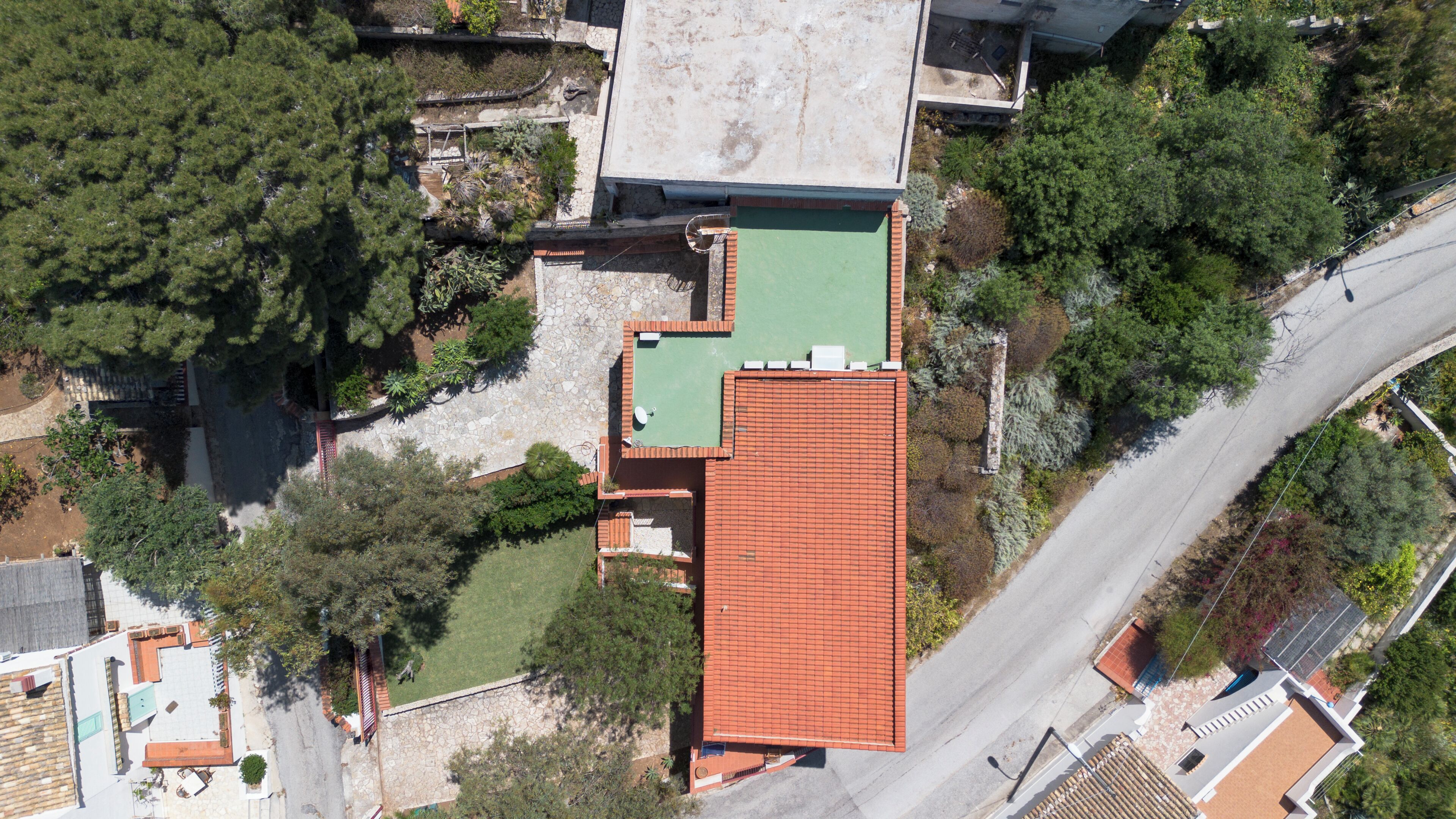 An aerial view of a residential property with a red-tiled roof, a green lawn, and surrounding trees.