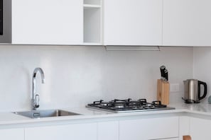 Een moderne keuken met een roestvrijstalen spoelbak, gasfornuis en waterkoker op het aanrecht.