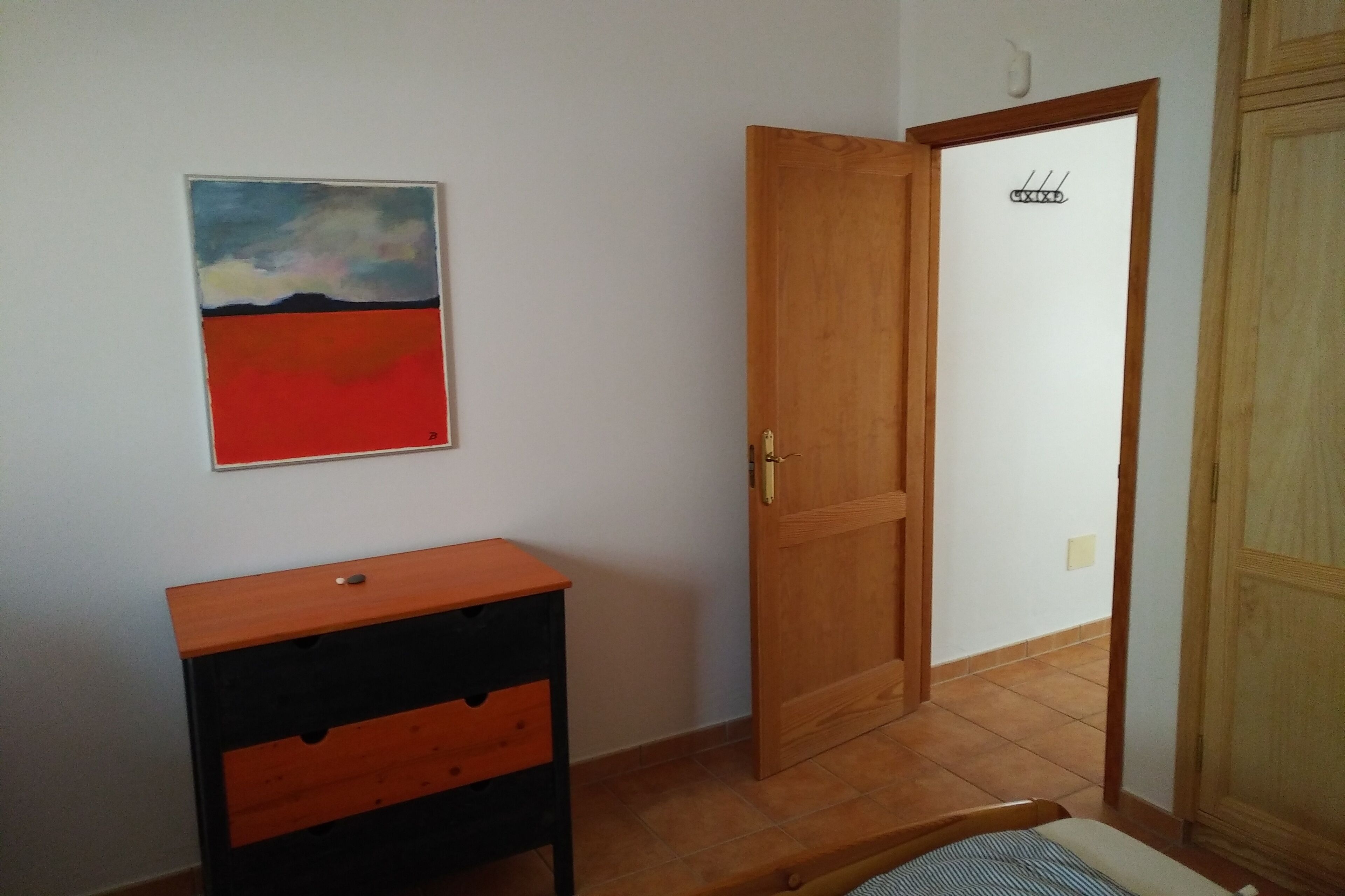 A room with a wooden door, a small wooden cabinet, and a painting on the wall.