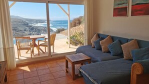 Een kamer met een grote schuifdeur die uitkomt op een terras met een tafel, stoelen, een bank en kunst aan de muur.