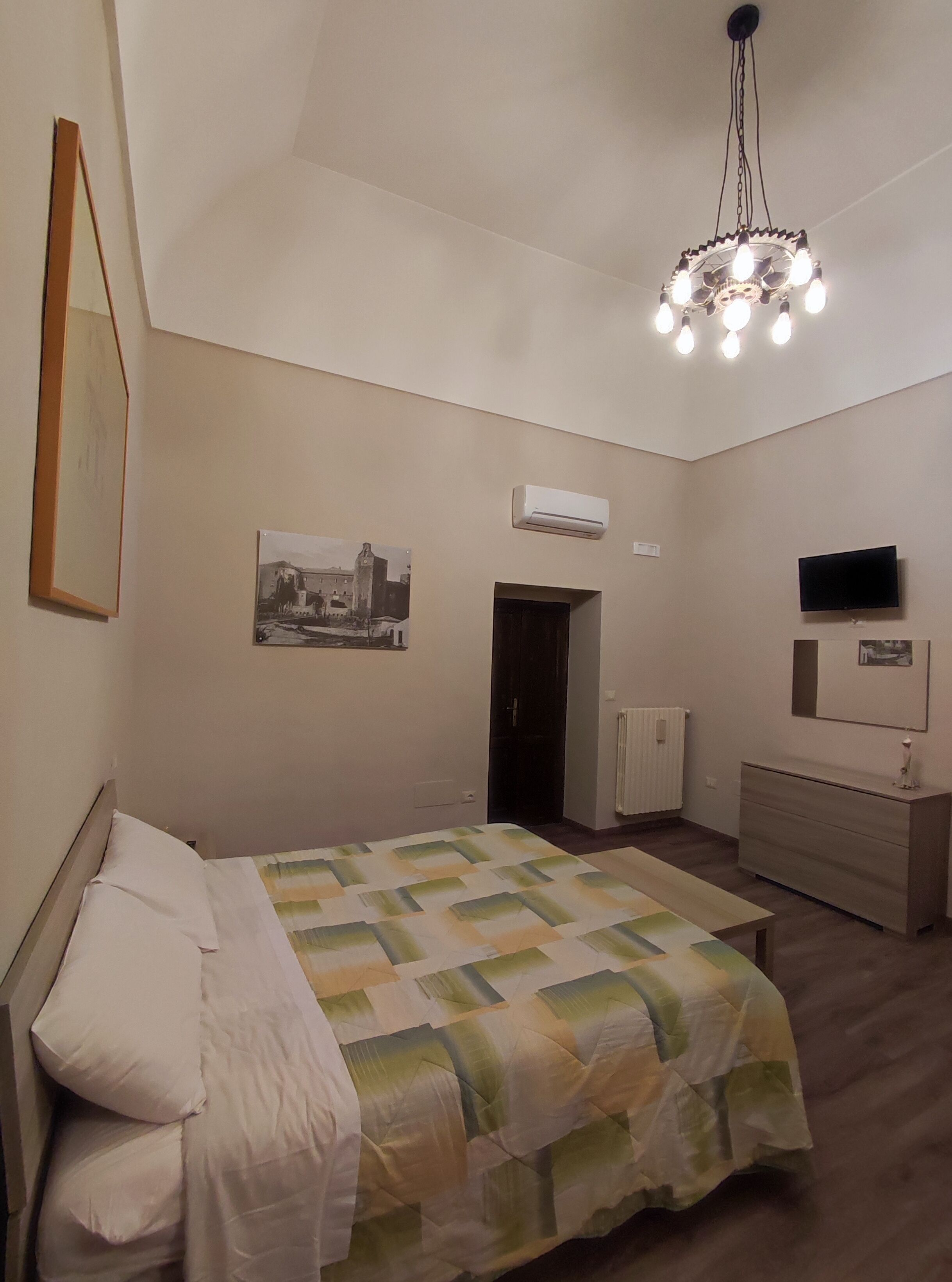 Una camera da letto con un letto, una cassettiera, una TV, un condizionatore d'aria e un lampadario.