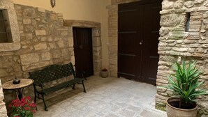 Un patio con suelo de piedra, una banca, una planta en maceta y una puerta.