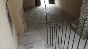 Una escalera estrecha de piedra con barandilla de metal, que conduce a un espacio abierto con vistas al interior de un edificio.