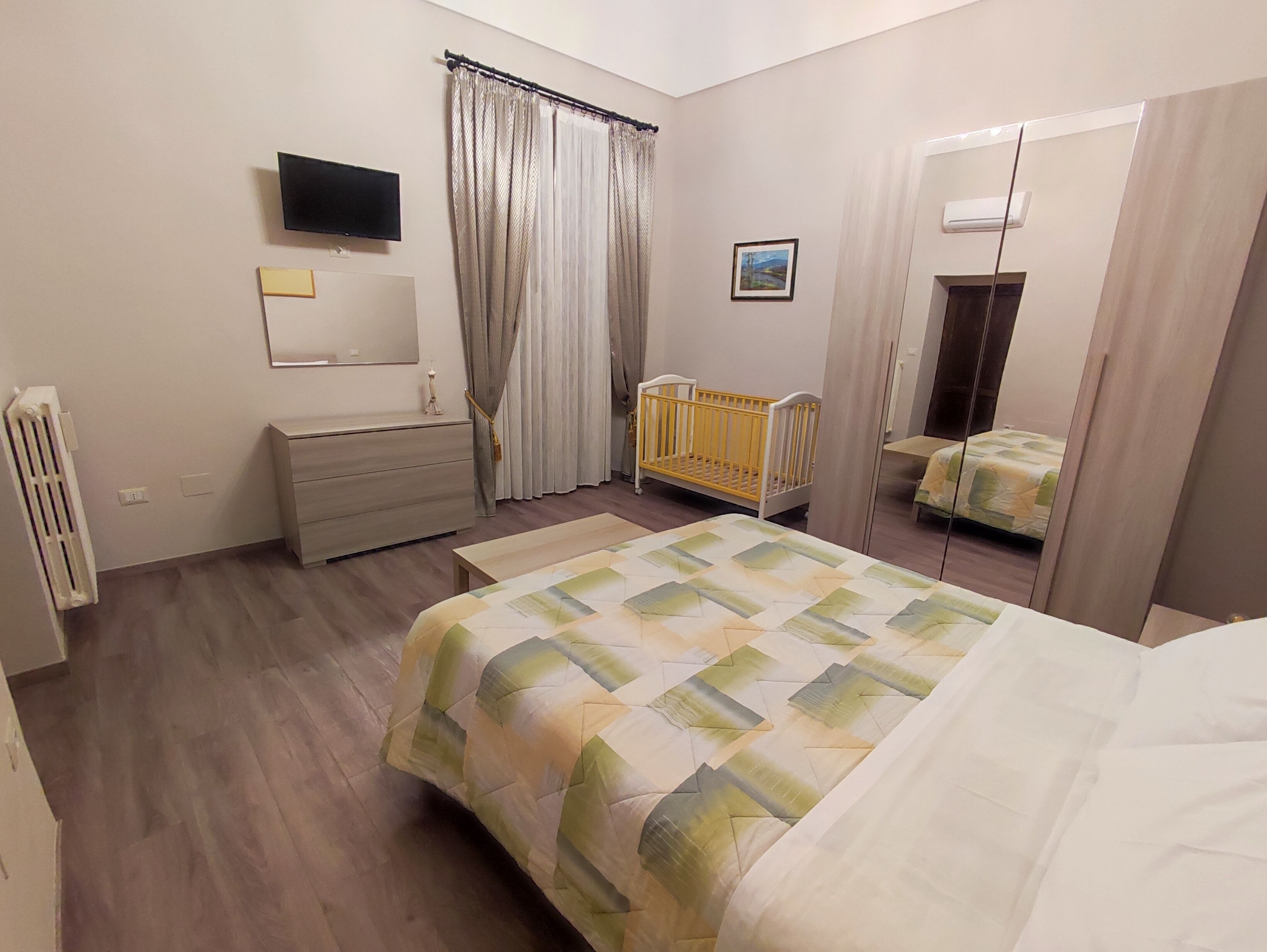 A bedroom with a bed, a crib, a dresser, a mirror, and a television.