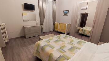 A bedroom with a bed, a crib, a dresser, a mirror, and a television.