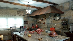A kitchen with a granite countertop, wooden cabinets, and stone walls. There are various kitchen utensils and cookware on the counter. - Douro and Tâmega - Quinta do Baroco  (Penafiel)