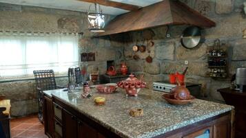 A kitchen with a granite countertop, wooden cabinets, and stone walls. There are various kitchen utensils and cookware on the counter.
