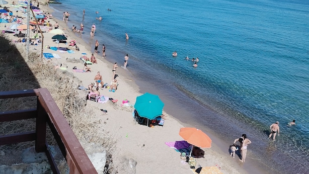 A beach with people sunbathing and swimming, a clear sky, and mountains in the background.