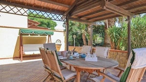 An outdoor patio with a wooden table and chairs, a green awning, and a stone wall.
