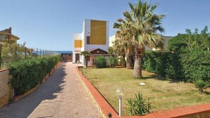 A pathway leading to a building with a modern design, surrounded by greenery and palm trees.