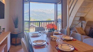 Ein Essbereich mit einem Tisch für vier Personen, einer Couch, einer Treppe und Blick auf Berge.