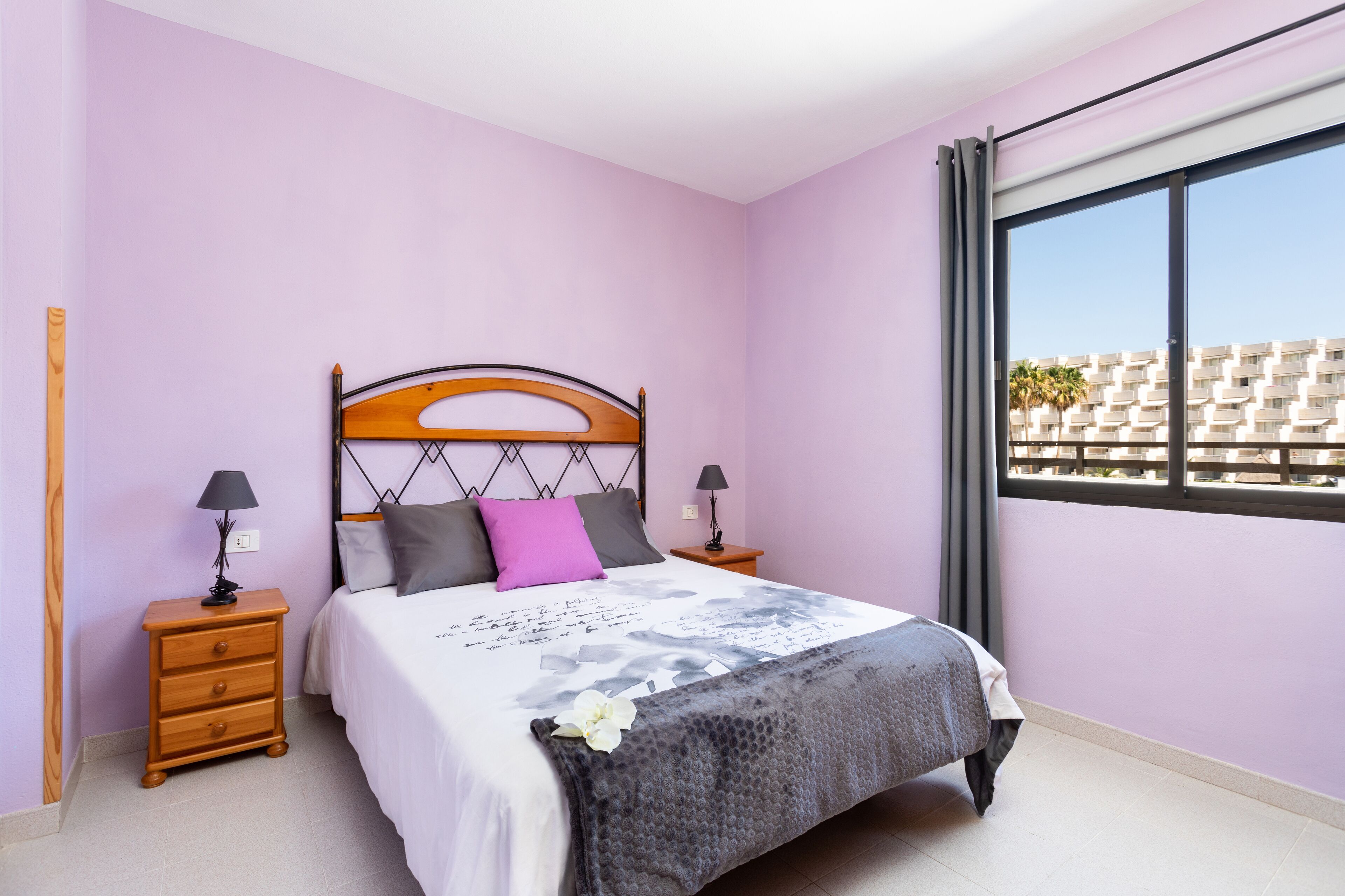 Una camera da letto con un letto, comodini, una finestra e vista sugli edifici.