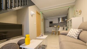 En moderne stue med et fladskærms-tv, en sofa og et spiseområde med et bord og stole.