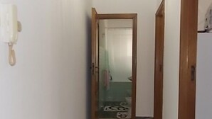 A narrow hallway with a wooden door at the end, a white wall, and a small rug on the floor.