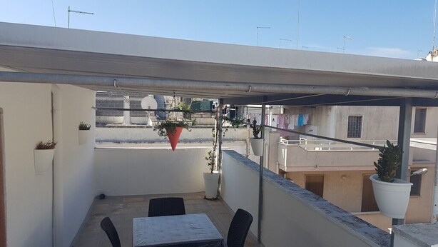 A rooftop terrace with a table and chairs, potted plants, and a view of the cityscape.