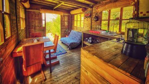 A rustic cabin with wooden walls and a wooden ceiling, a dining area with a table and chairs, a sofa, and a kitchen area with a sink and a large water container. - Cabaña Agrreste Bed & Breakfast (Nemocón)