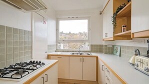 Une cuisine de taille réduite, équipée d’une cuisinière à gaz, d’un évier et de meubles de rangement en bois.